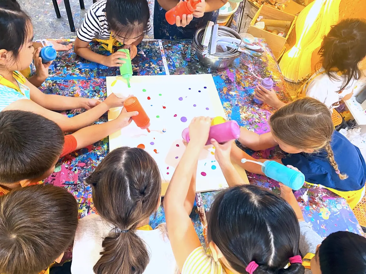 Overhead view of kids pouring colorful paint at holiday art camp