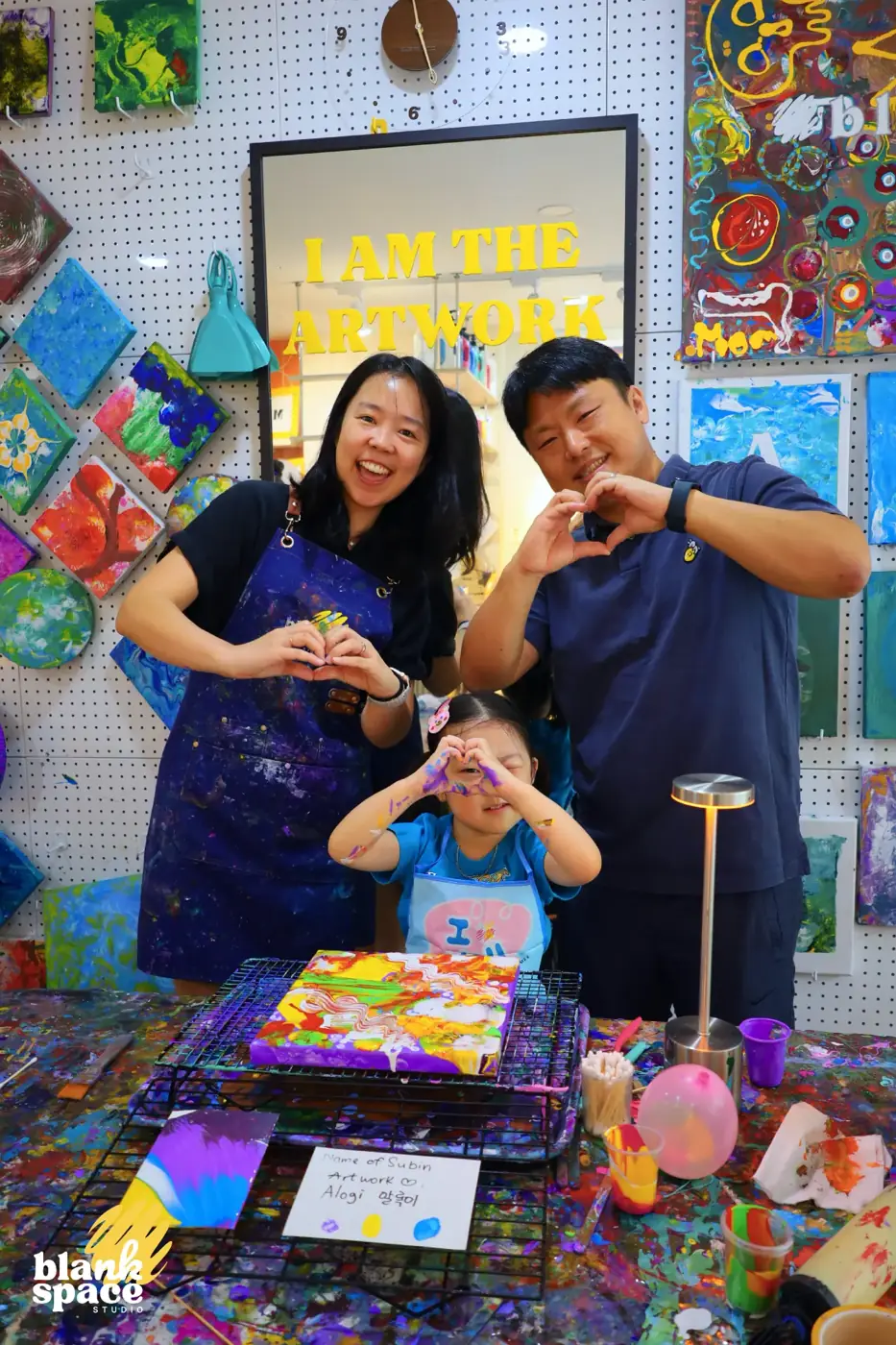 Parents and daughter making heart signs beside their artwork