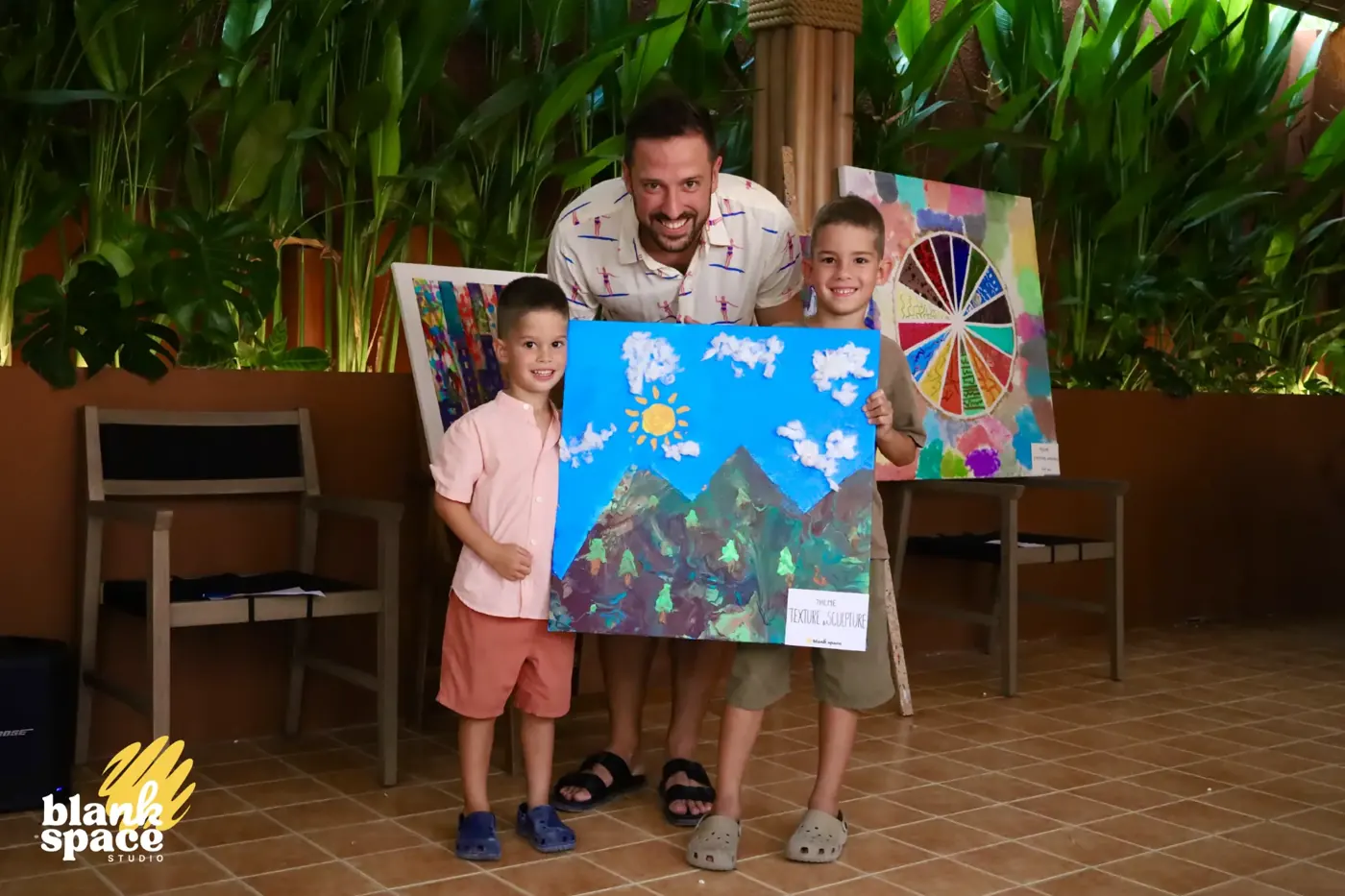 Dad and two boys holding a mountain landscape canvas at the charity auction