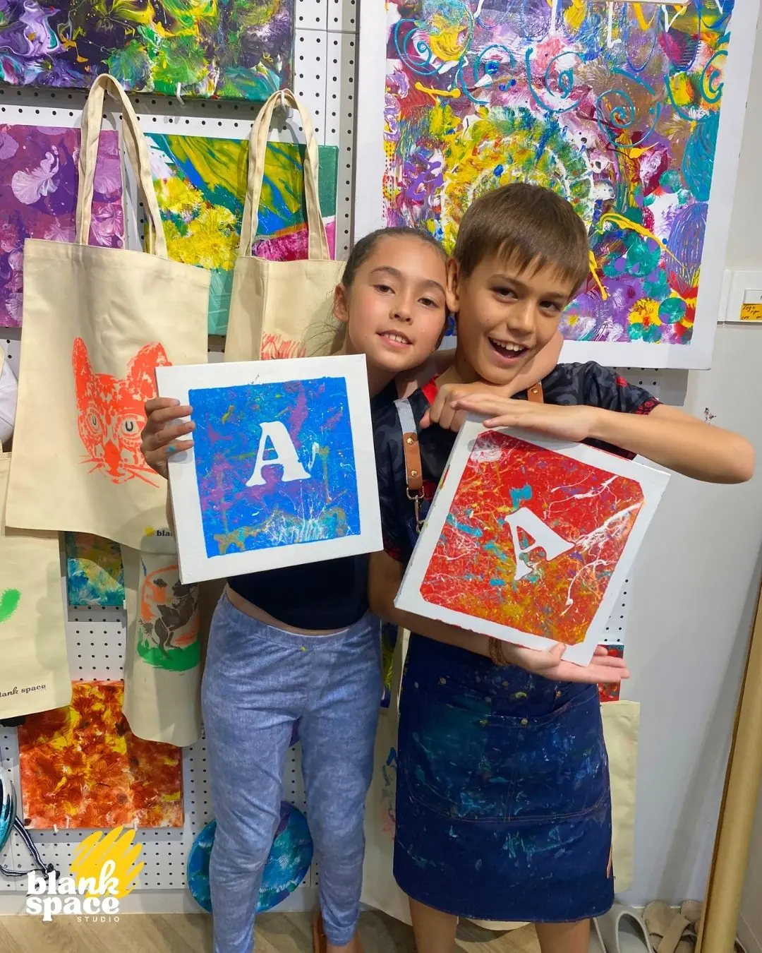Siblings holding stencil art canvases at a kids birthday venue near Thao Dien