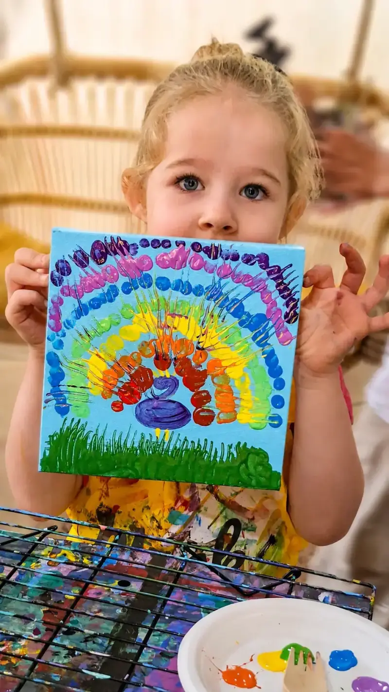 Young camper holding her rainbow canvas at a kids art camp