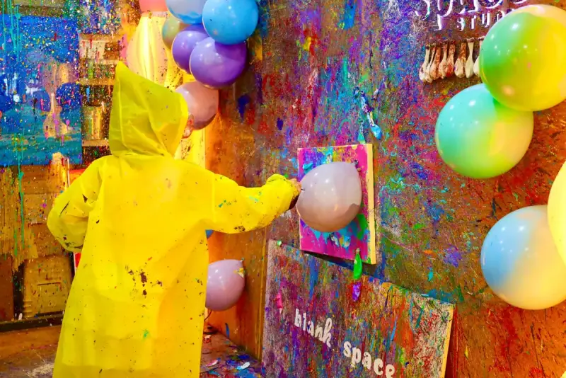 Child in a yellow poncho popping paint balloons at a birthday party in Saigon