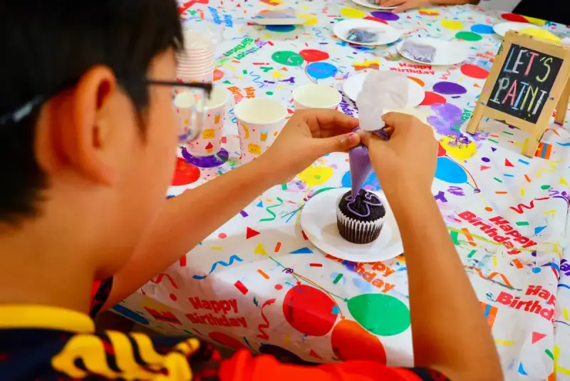 Child piping icing on a cupcake at a birthday party at Blank Space Studio
