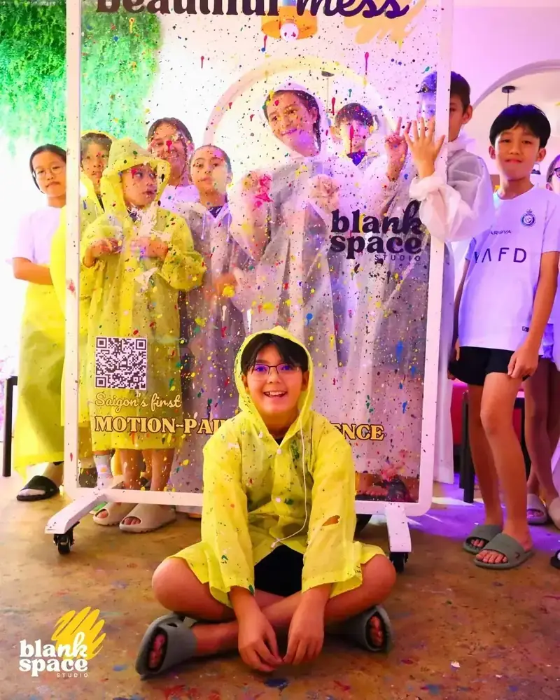 Kids in yellow ponchos posing at a paint-splatter birthday party at Blank Space Studio Saigon