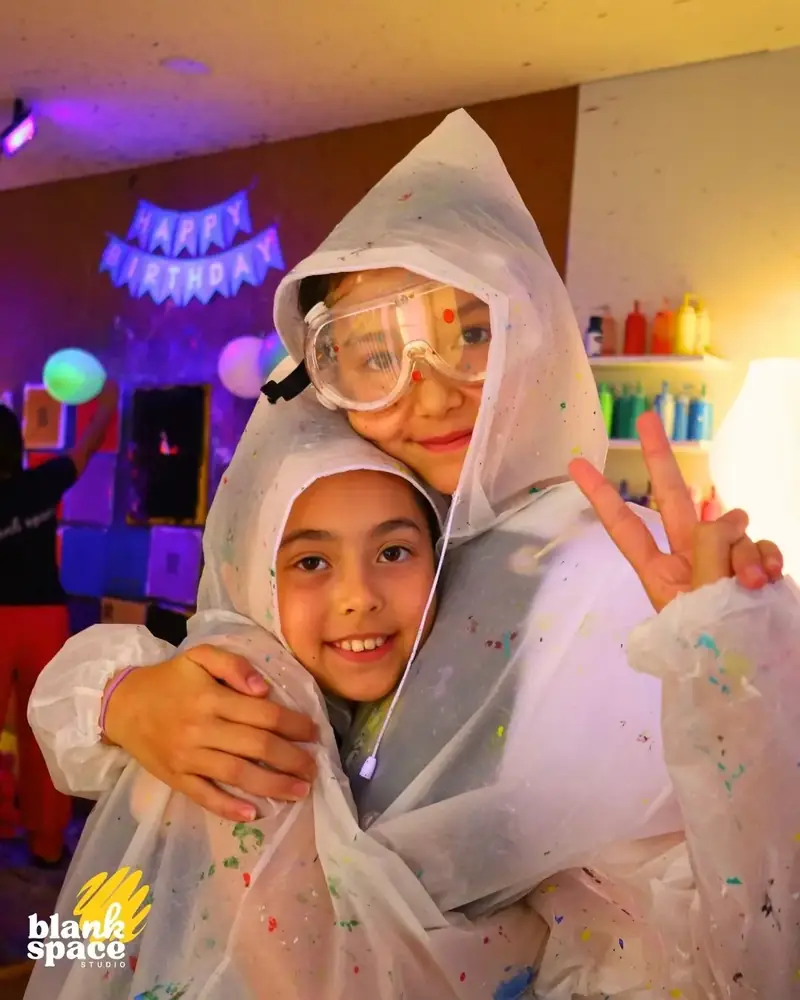 Two kids hugging in paint ponchos at a birthday party at Blank Space Studio