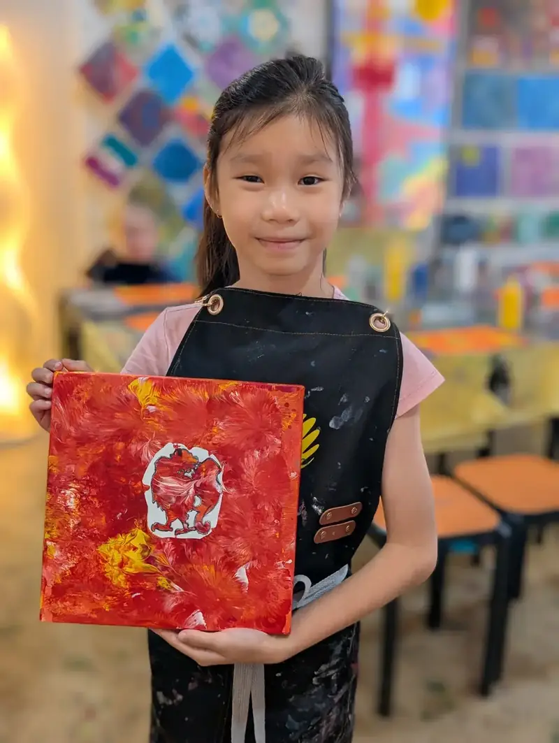 Girl proudly holding red abstract canvas at a paint pouring camp in HCMC