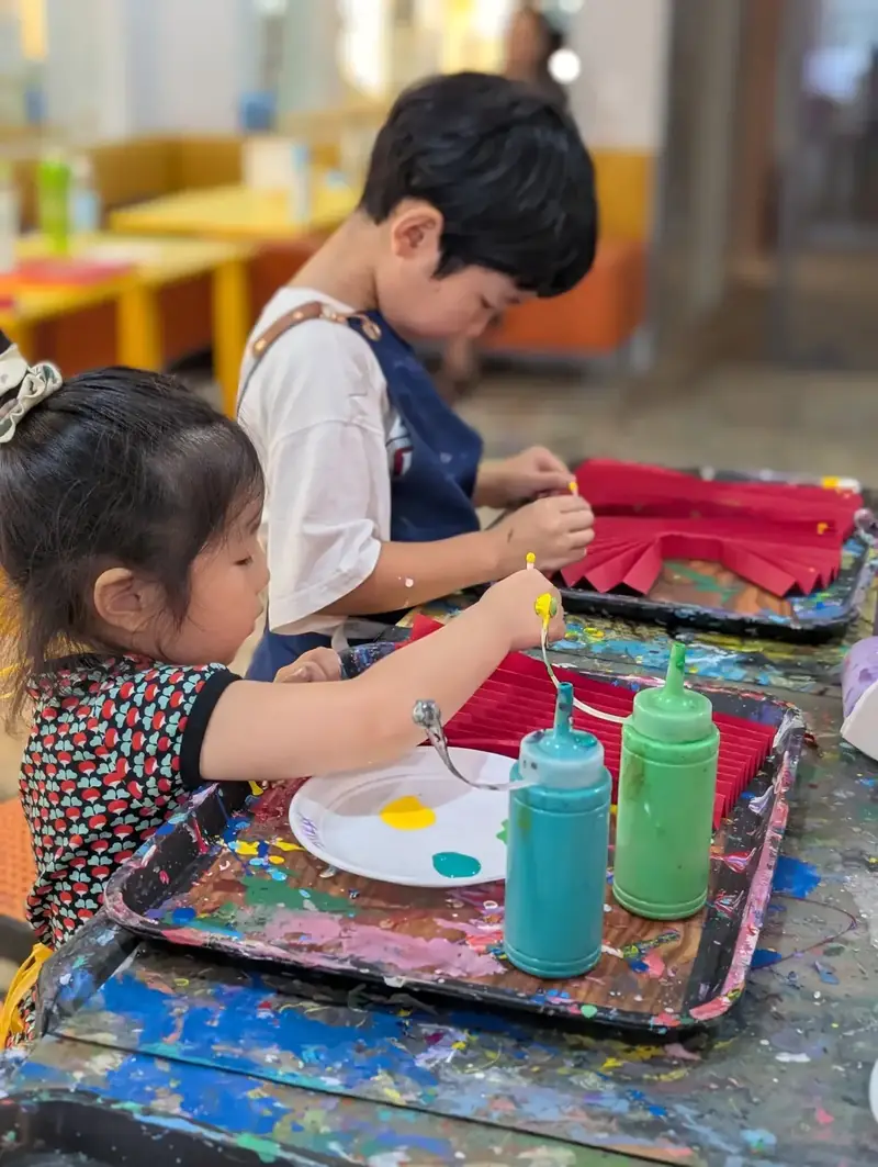 Kids painting red paper fans at an art camp near Thao Dien