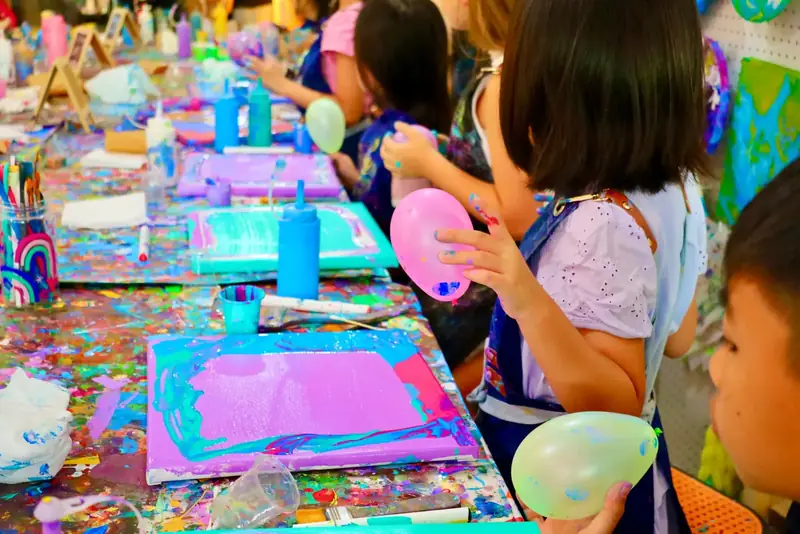 Kids using balloons as painting tools on canvases at an art workshop