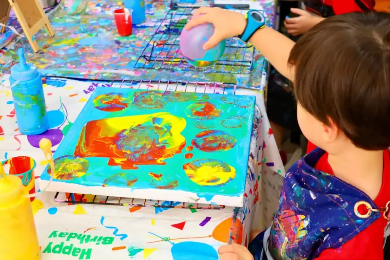 Boy using motion and a balloon to create a colorful fluid art canvas