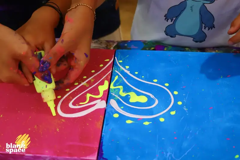 Two friends painting matching neon canvases side by side