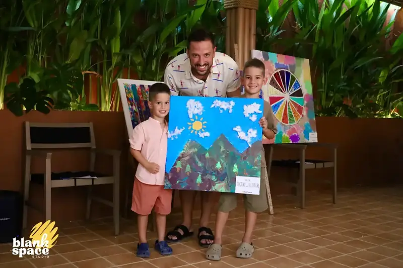 Dad and two boys holding a mountain landscape canvas at the charity auction