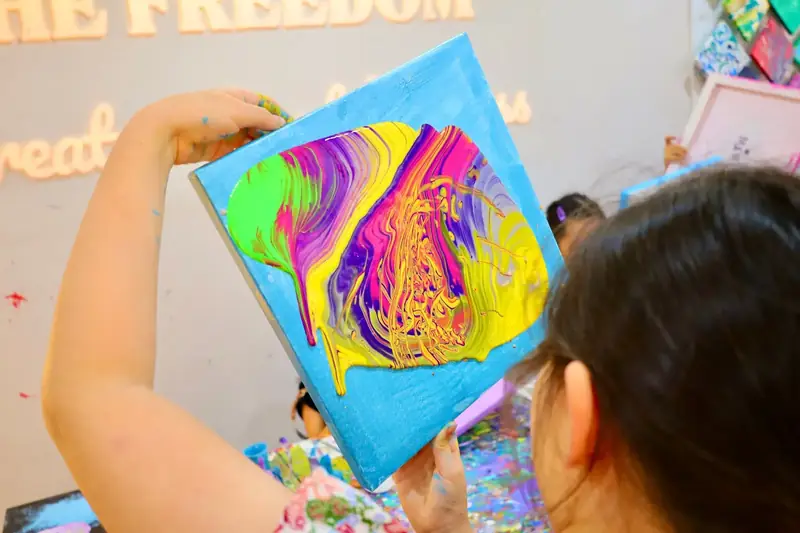Child holding up a bright abstract fluid art canvas at a celebration in HCMC