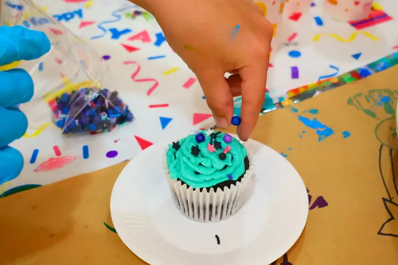Guest decorating a cupcake with sprinkles at a creative celebration party