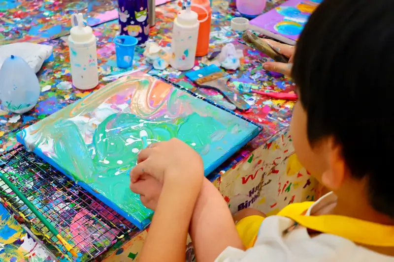 Child creating a swirled fluid art canvas at a creative celebration in HCMC