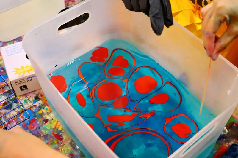 Water marbling tray with red and blue paint at a creative celebration near Thao Dien