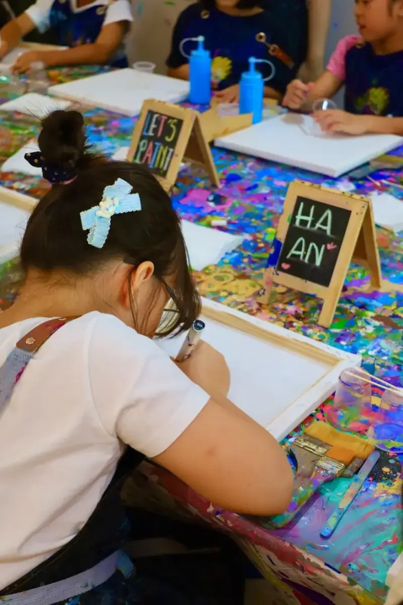 Child writing her name on a personalised canvas at a private studio event in Saigon