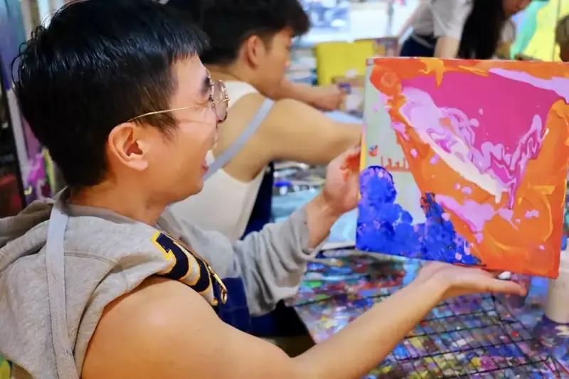 Guest smiling with a pink and orange pour painting at an evening session