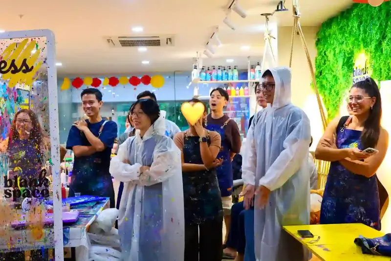 Team in aprons and ponchos laughing during a messy paint team bonding activity in Saigon