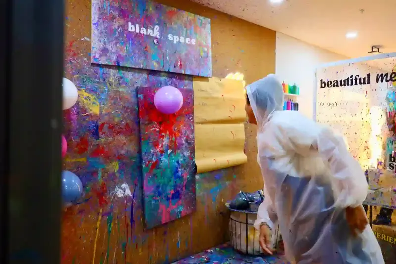 Guest in a rain poncho popping a paint balloon on the splatter wall at a team bonding event in Saigon